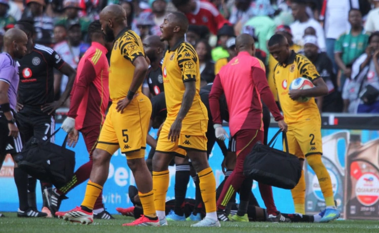 Kaizer Chiefs midfielders Sibongiseni Mthethwa and Lebohang Maboe walk past an injured Tshepang Moremi of Orlando Pirates
